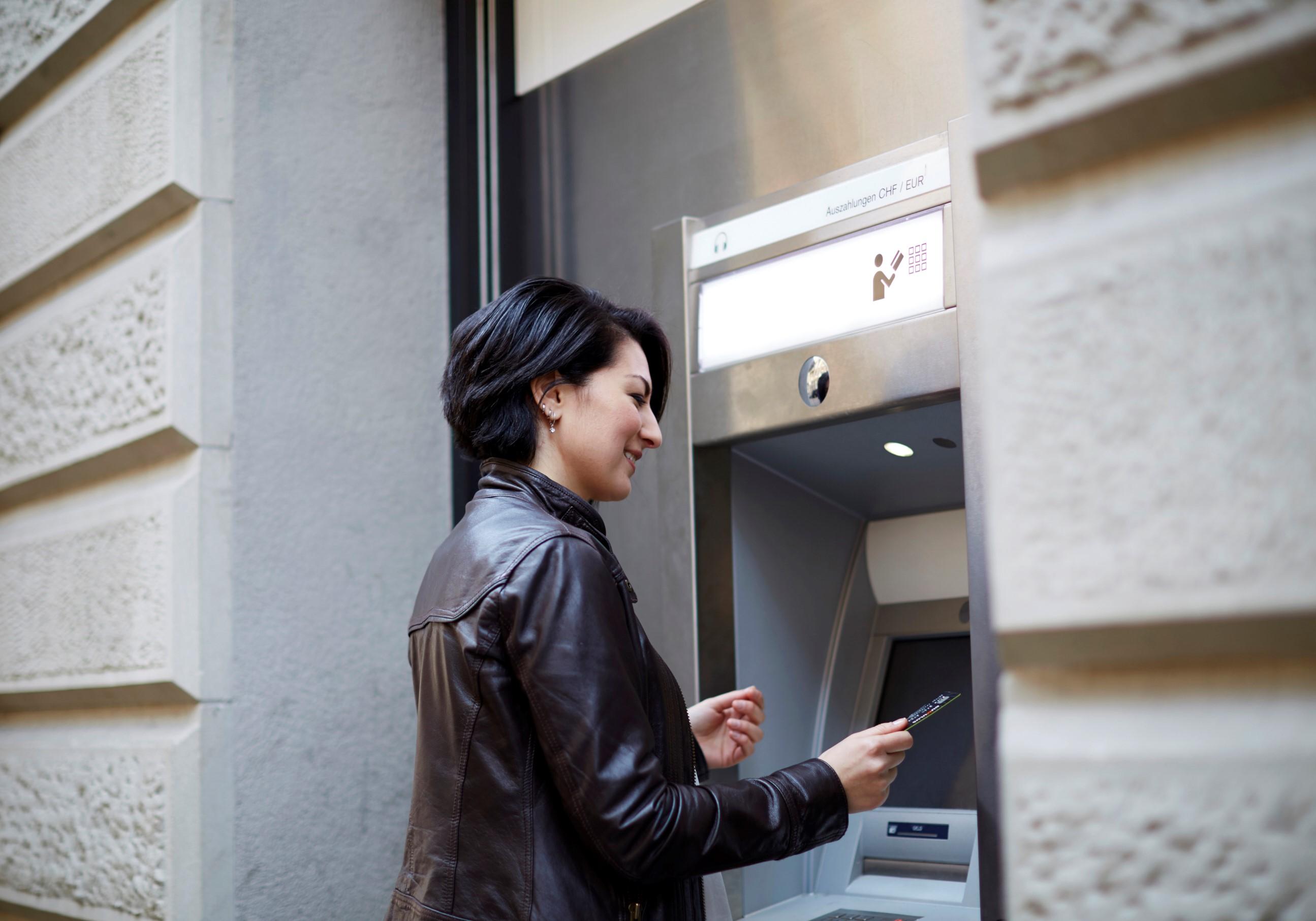 Une femme se tient devant un distributeur automatique de billets.