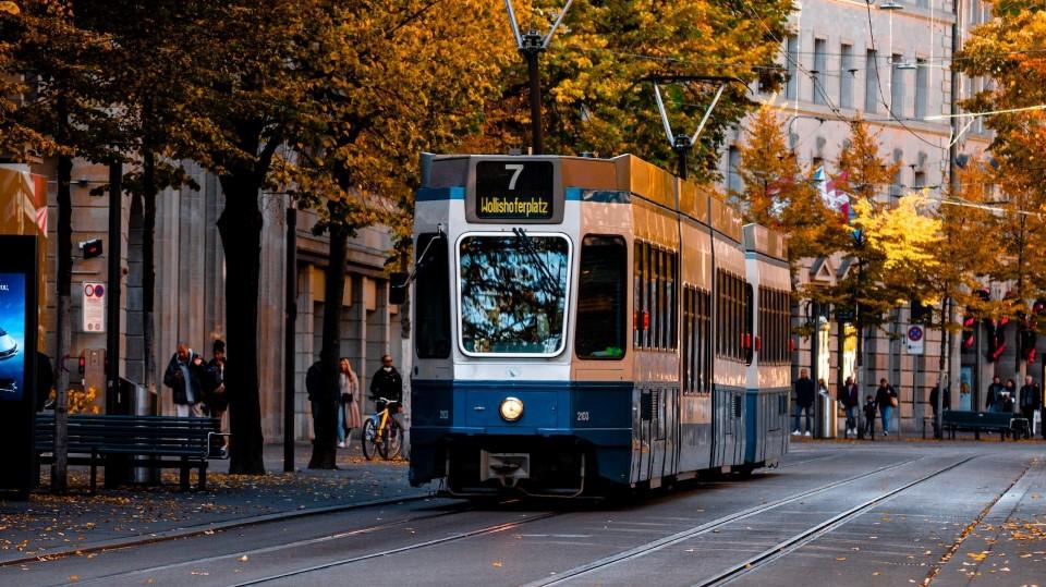 Un tram zurichois bleu et blanc traverse la rue.