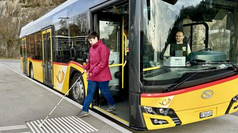 Eine Person mit weissem Stock steigt aus einem Postauto.