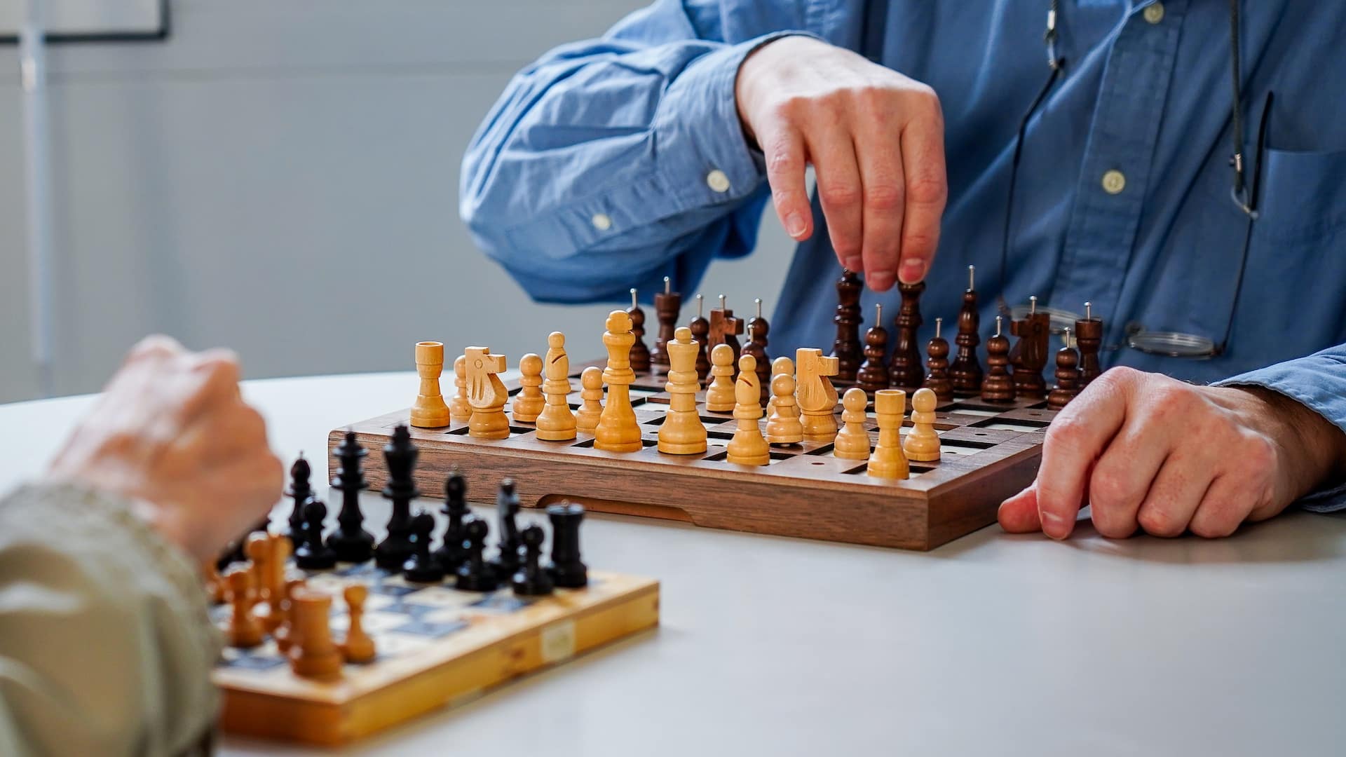 Gros plan: deux cases d'échecs sont placées sur une table. Les joueurs sont assis devant ou derrière et saisissent les pièces d'échecs avec leurs mains.