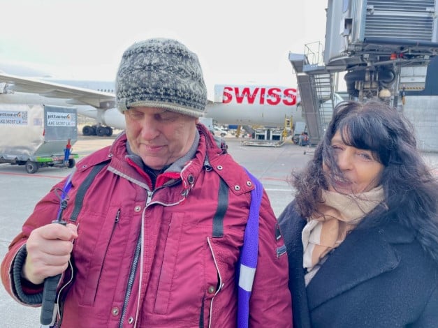 Das BBZ Zürich auf dem Flughafen Zürich: Ein blinder Mann mit Gehstock, belgeitet durch eine Frau mit langen, schwarzen Haaren stehen auf dem Rollfeld des Flughafens. Im Hintergrund rollt eine Swiss-Maschine vorbei.