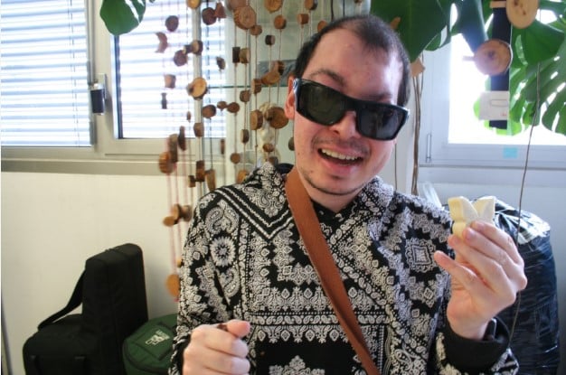 Handwerk im BBZ Zürich: Ein junger, blinder Mann mit Dunkelbrille zeigt lachend einen aus Speckstein angefertigten Schmetterling.