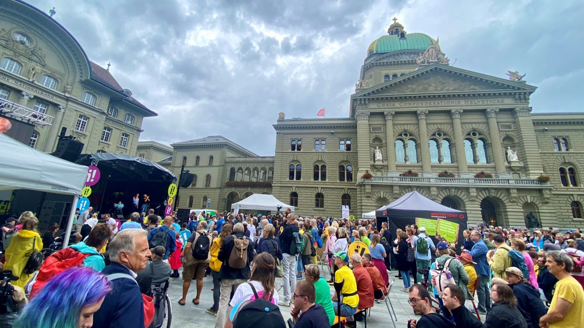 Rund 1000 Menschen haben sich auf dem Bundesplatz in Bern versammelt, sie tragen Regenjacken und haben Schirme dabei.