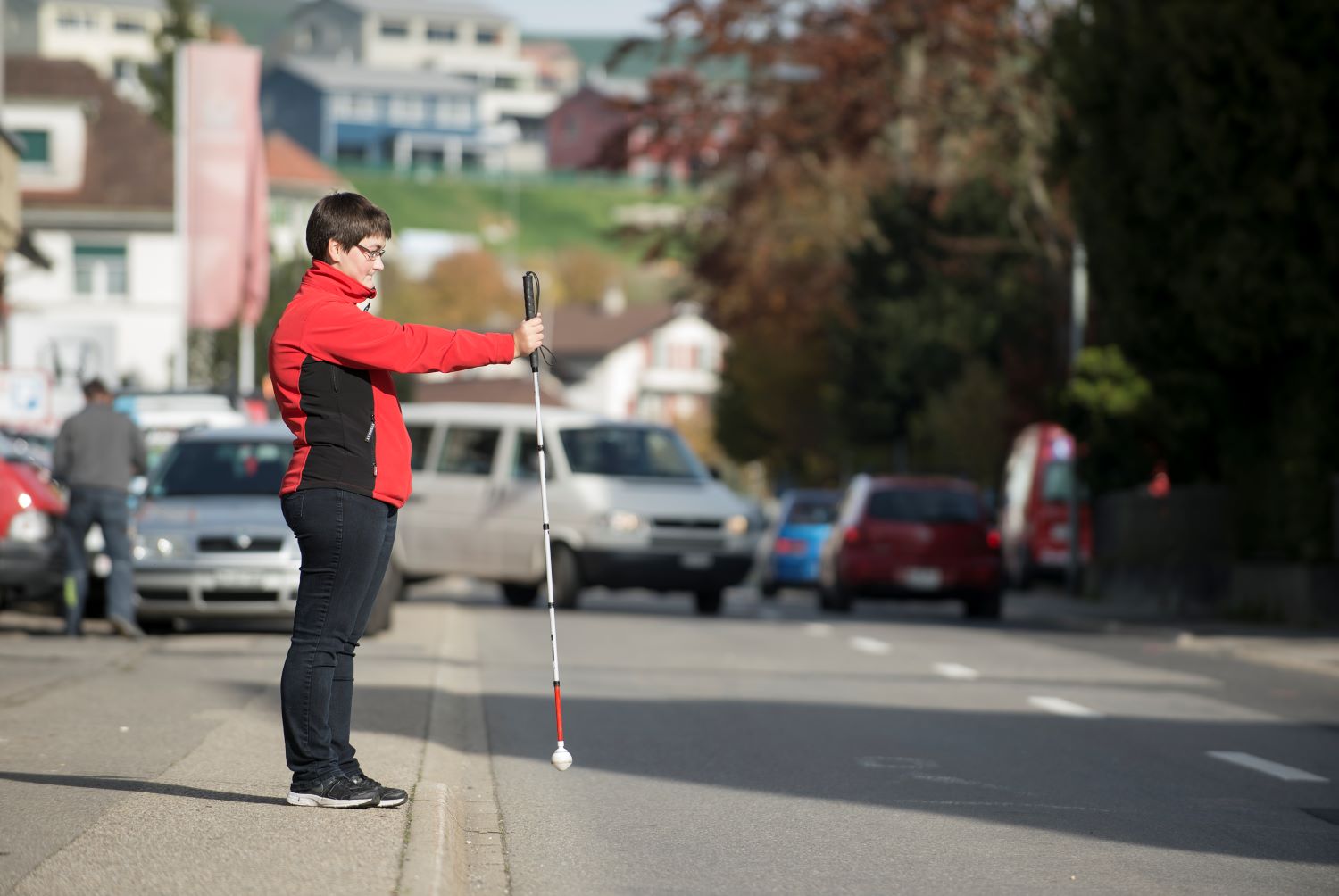 Une femme avec une canne blanche se tient au bord de la route