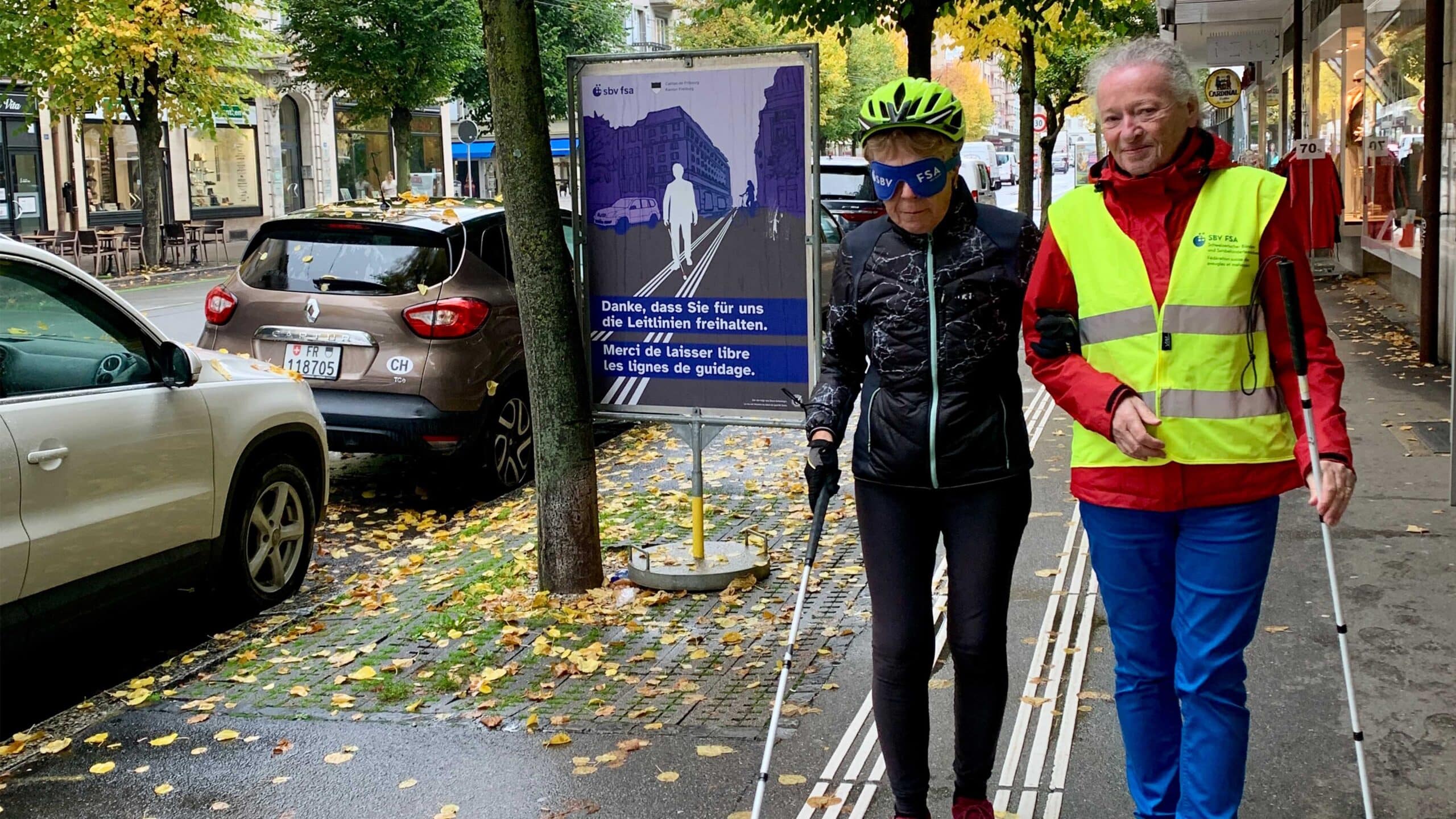 Eine Person führt eine sehbehinderte Person über die Leitlinien.