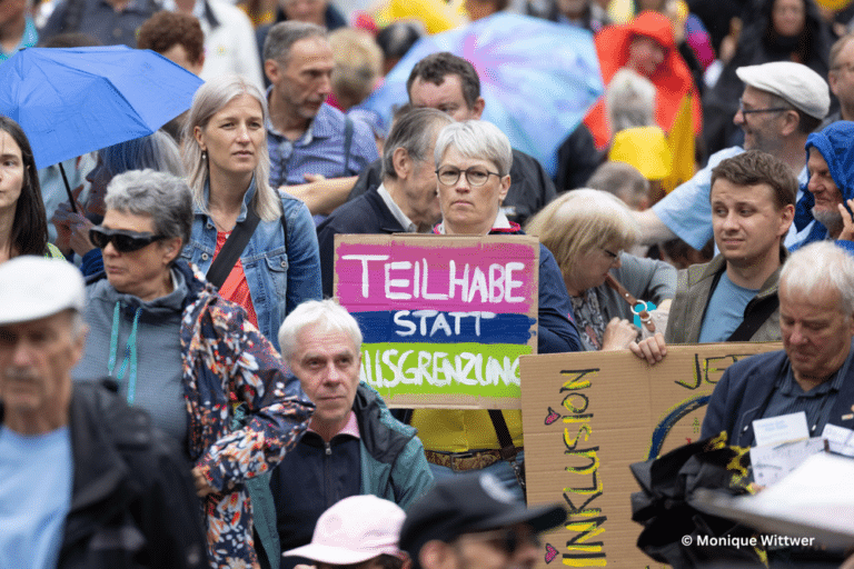 Menschenmenge, eine Person hält ein Schild hoch: "Teilhabe statt Ausgrenzung"