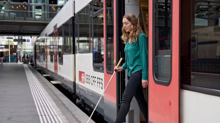 Une femme avec une canne blanche descend d'un train CFF