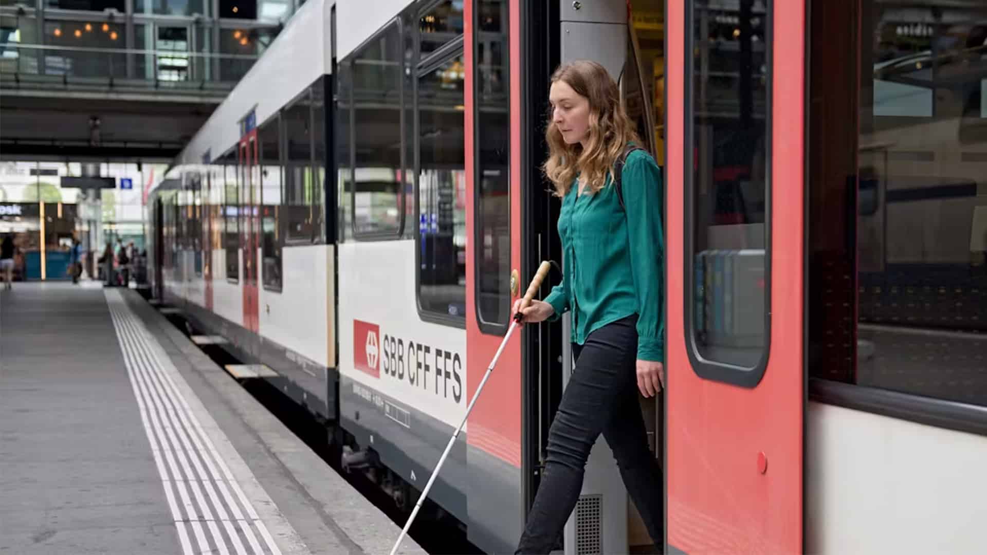 Une femme avec une canne blanche descend d'un train CFF