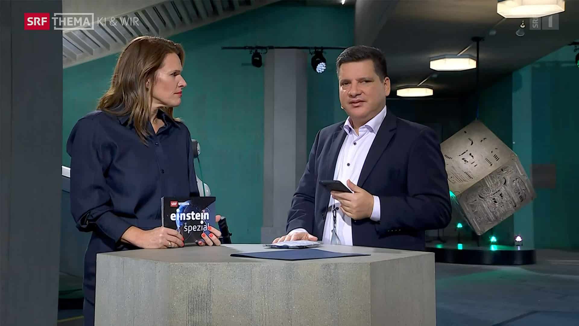 La photo montre la présentatrice de la SRF Kathrin Hönegger interviewant Luciano Butera.En arrière-plan, on peut voir les locaux de l'EPF de Zurich.