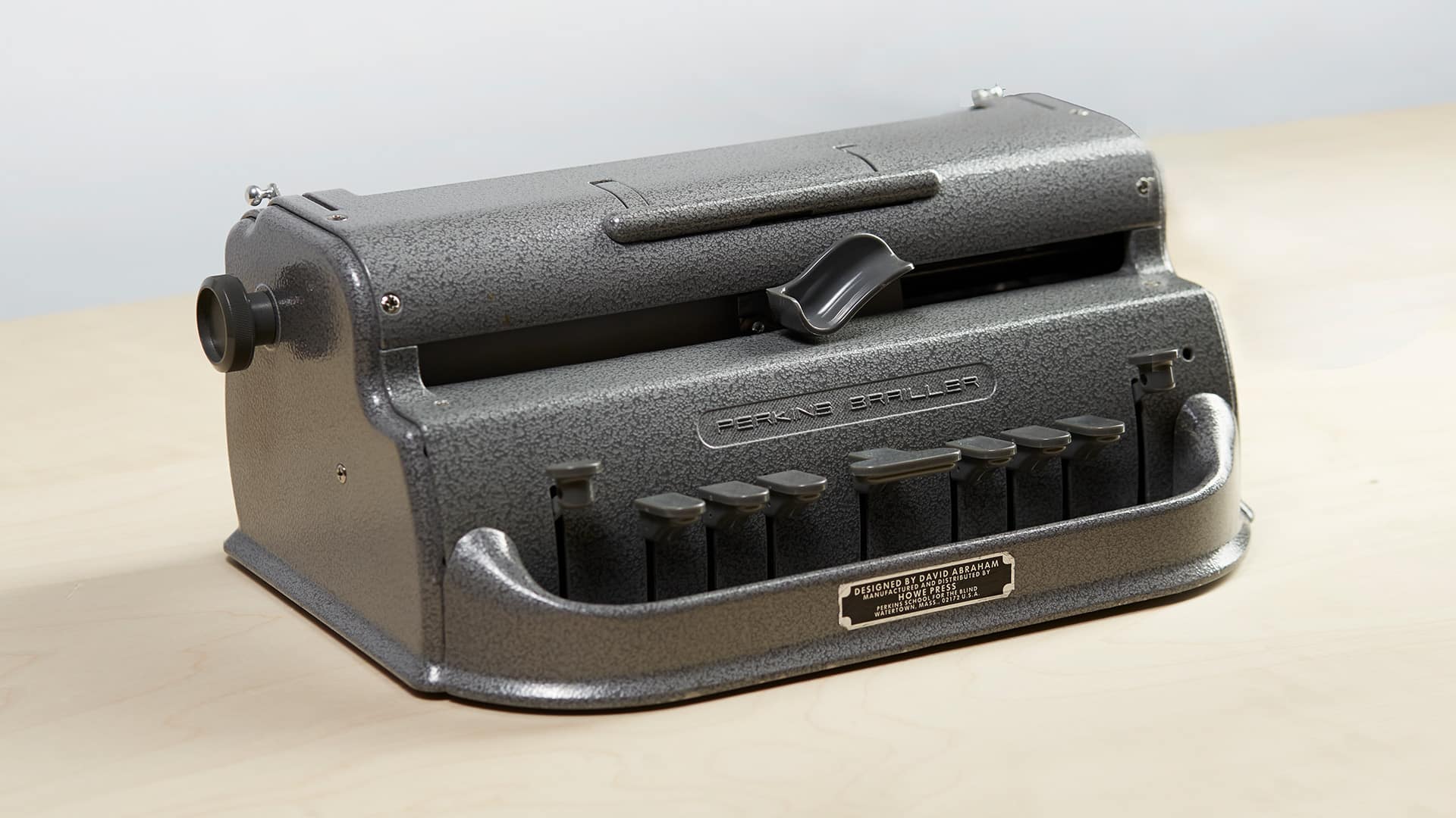 L'image montre une machine à écrire en braille sur une table en bois.