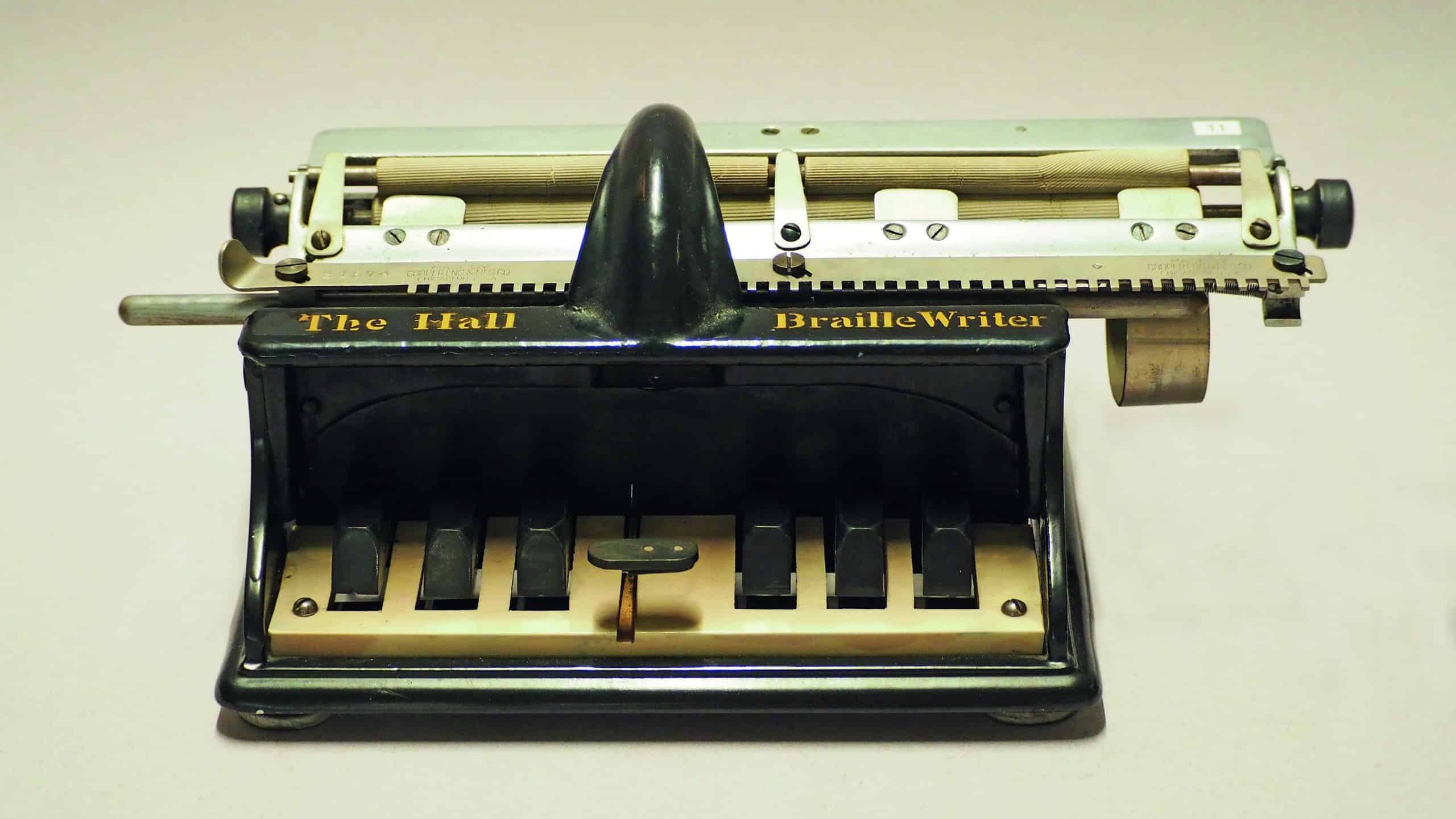 Photo de la première machine à écrire braille datant de 1882. Sur la face avant se trouvent les 6 touches caractéristiques et en haut l'énorme chariot d'impression. Une inscription dorée indique. «The Hall Braille Writer».