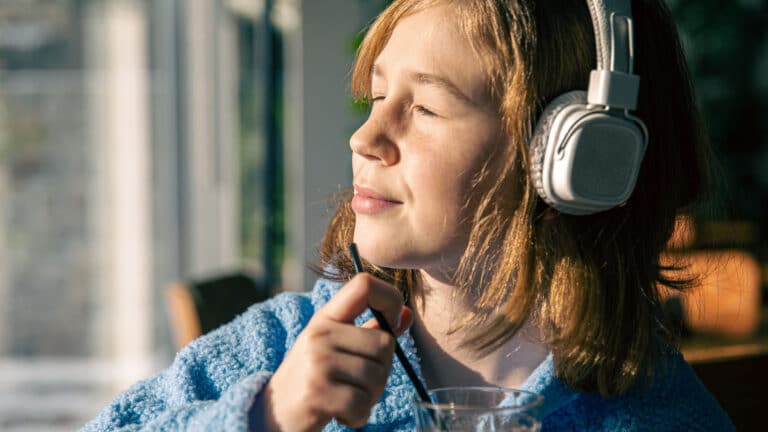 Junge Frau mit weissen Kopfhörern hält ihr Gesicht mit geschlossenen Augen in die Sonne