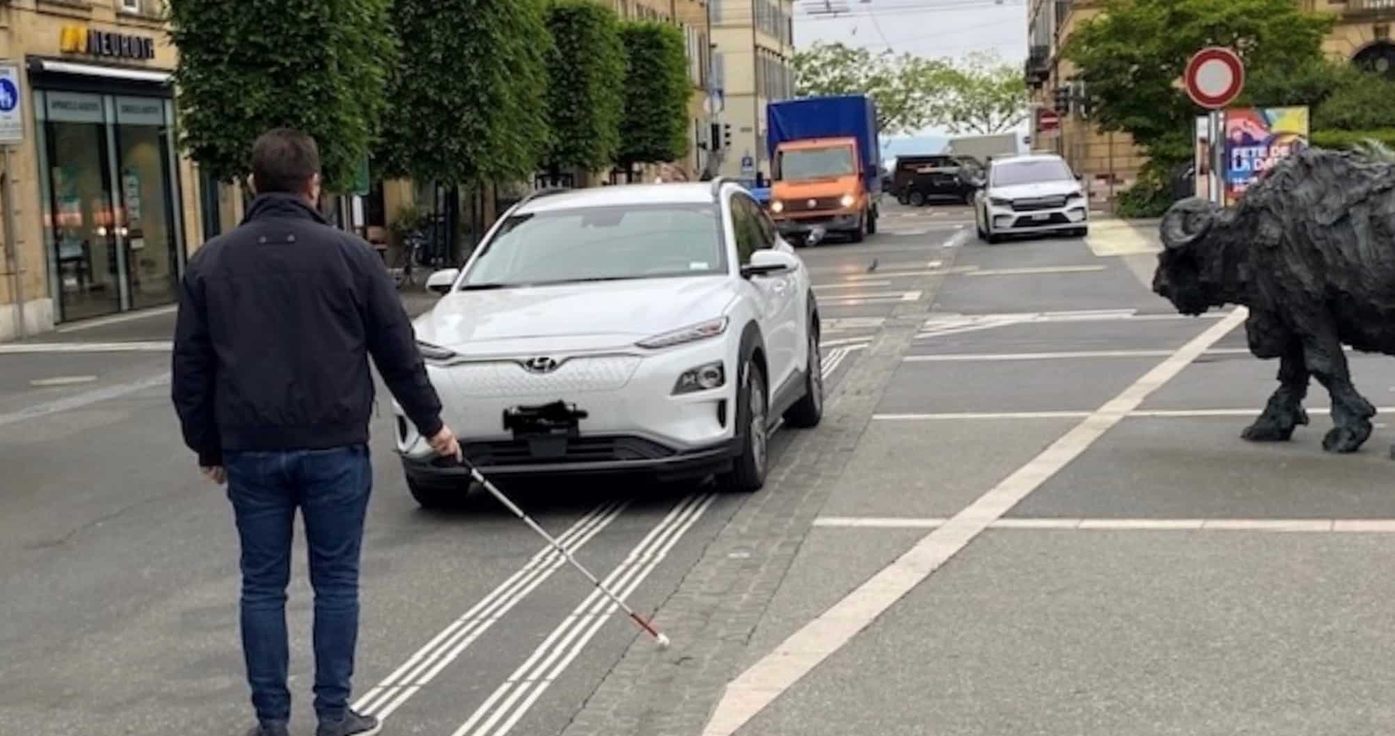 Place Pury /NE: homme, canne blanche et voiture électrique mal garée.