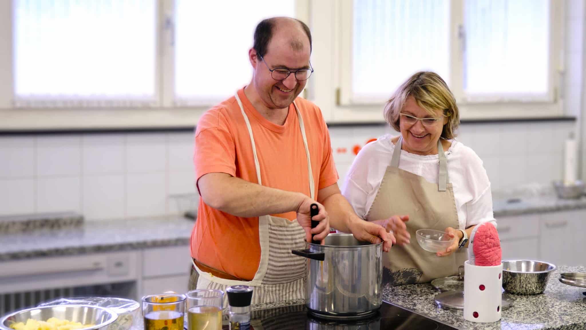 Ein Mann und eine Frau an einer Küchenzeile, er rührt in einem grossen Topf. Foto aus einem Kochkurs des sbv