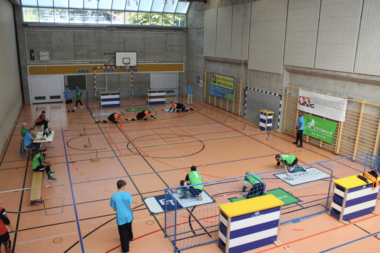 Eine Turnhalle mit zwei spielenden Torballteams und einigen Zuschauenden.