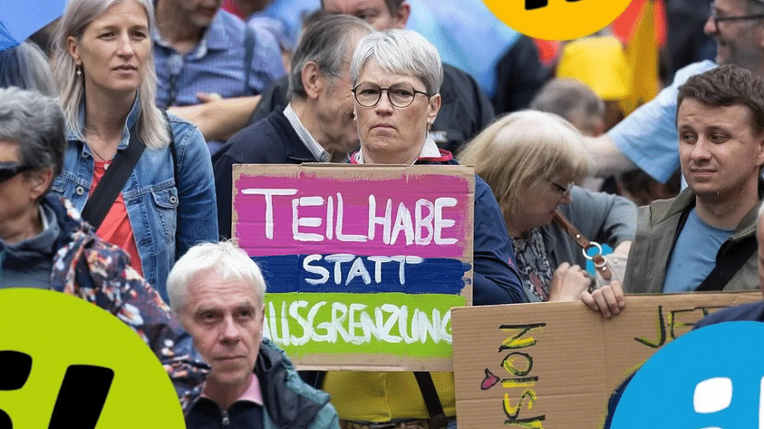 Femme dans une foule de manifestants avec une pancarte "La participation plutôt que l'exclusion".