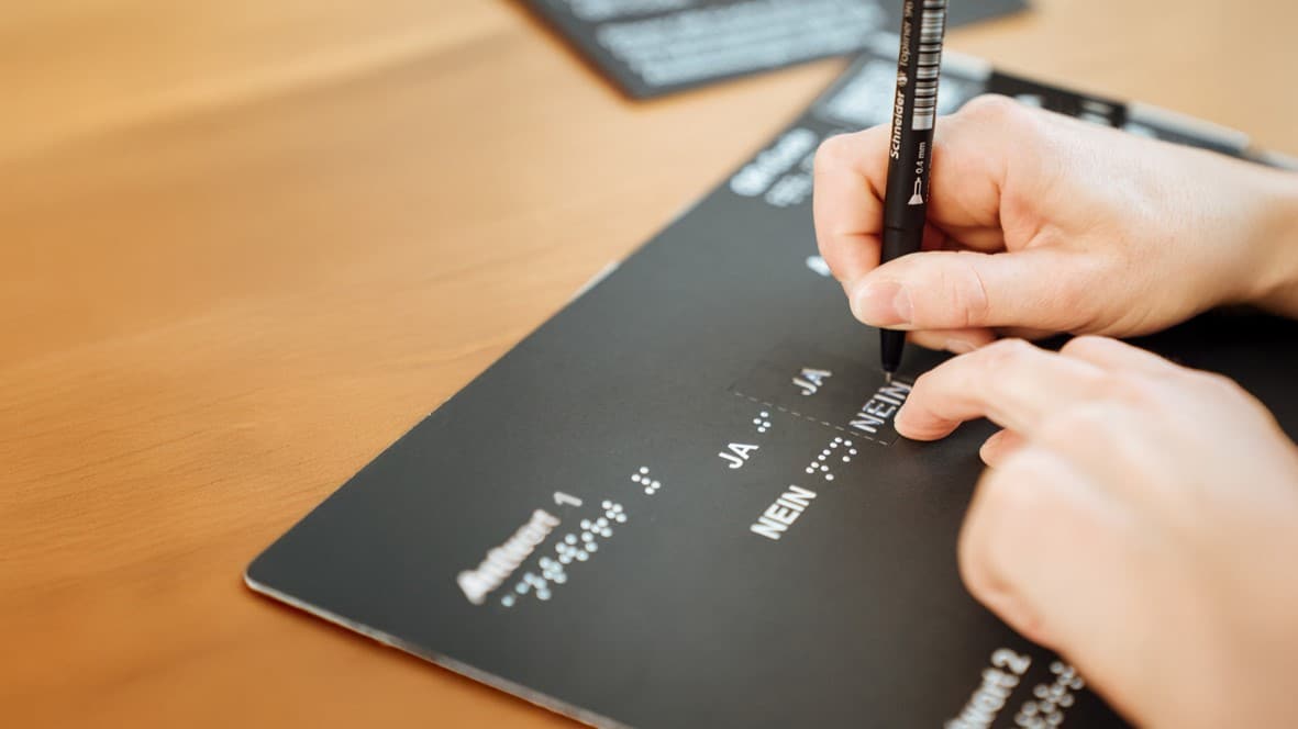 Abstimmungsschablone, man sieht eine Hand mit Stift, die dem Wort "Nein" n der Schreibvorlage nachfährt