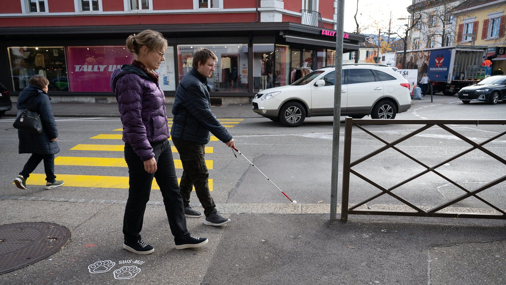 Ein junger Mann mit weissem Stock wird von seiner O&M-Beraterin begleitet.
