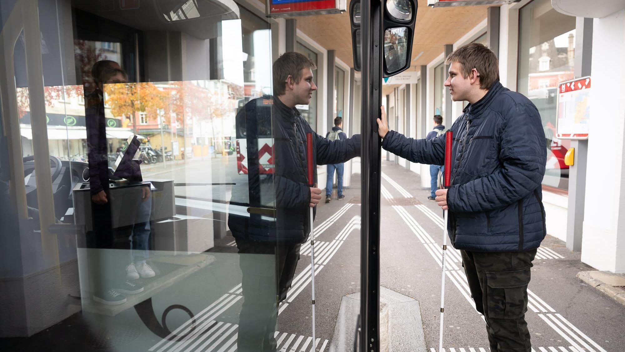 Ein junger Mann mit weissem Stock steigt in einen Bus ein.