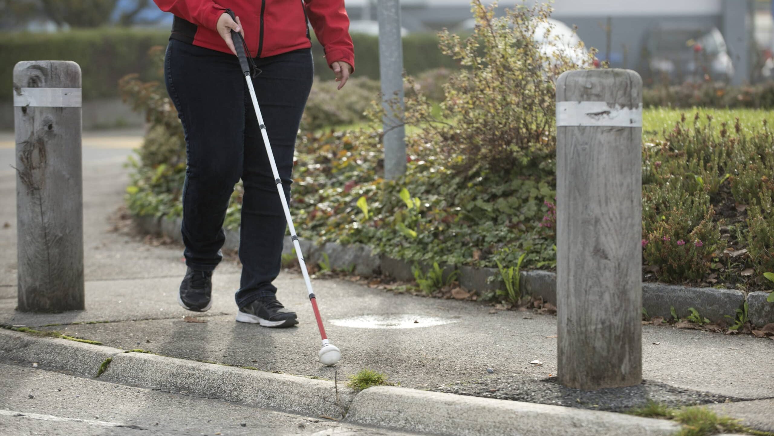Eine Person orientiert sich mit einem weissen Stock entlang des Trottoirrands.