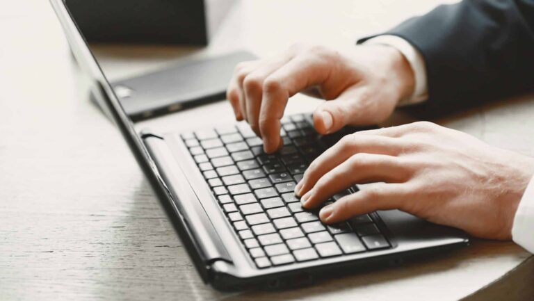 Zwei Hände tippen auf der Tastatur eines Laptops (Nahaufnahme).