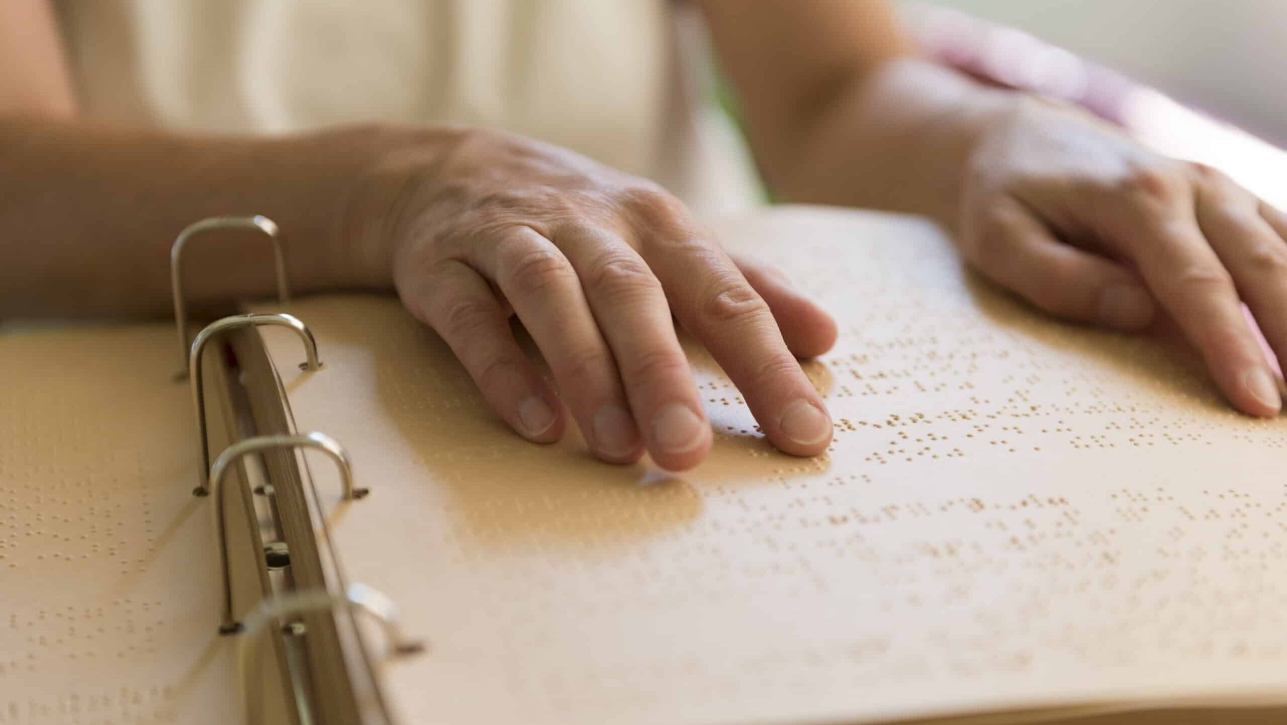 Zwei Hände ertasten die Brailleschrift in einem geöffneten Ordner.