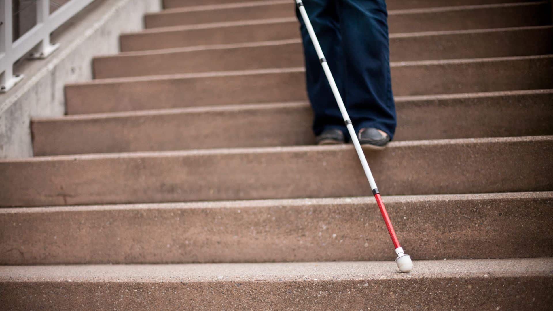 Les jambes d'une personne munie d'une canne blanche dans un escalier