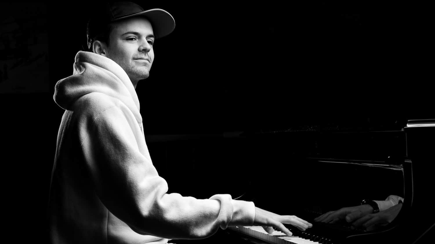Loris Mittaz spielt am Flügel. Schwarzweiss-Foto. Loris Mittaz trägt einen weissen Kapuzenpulli und ein Cap.