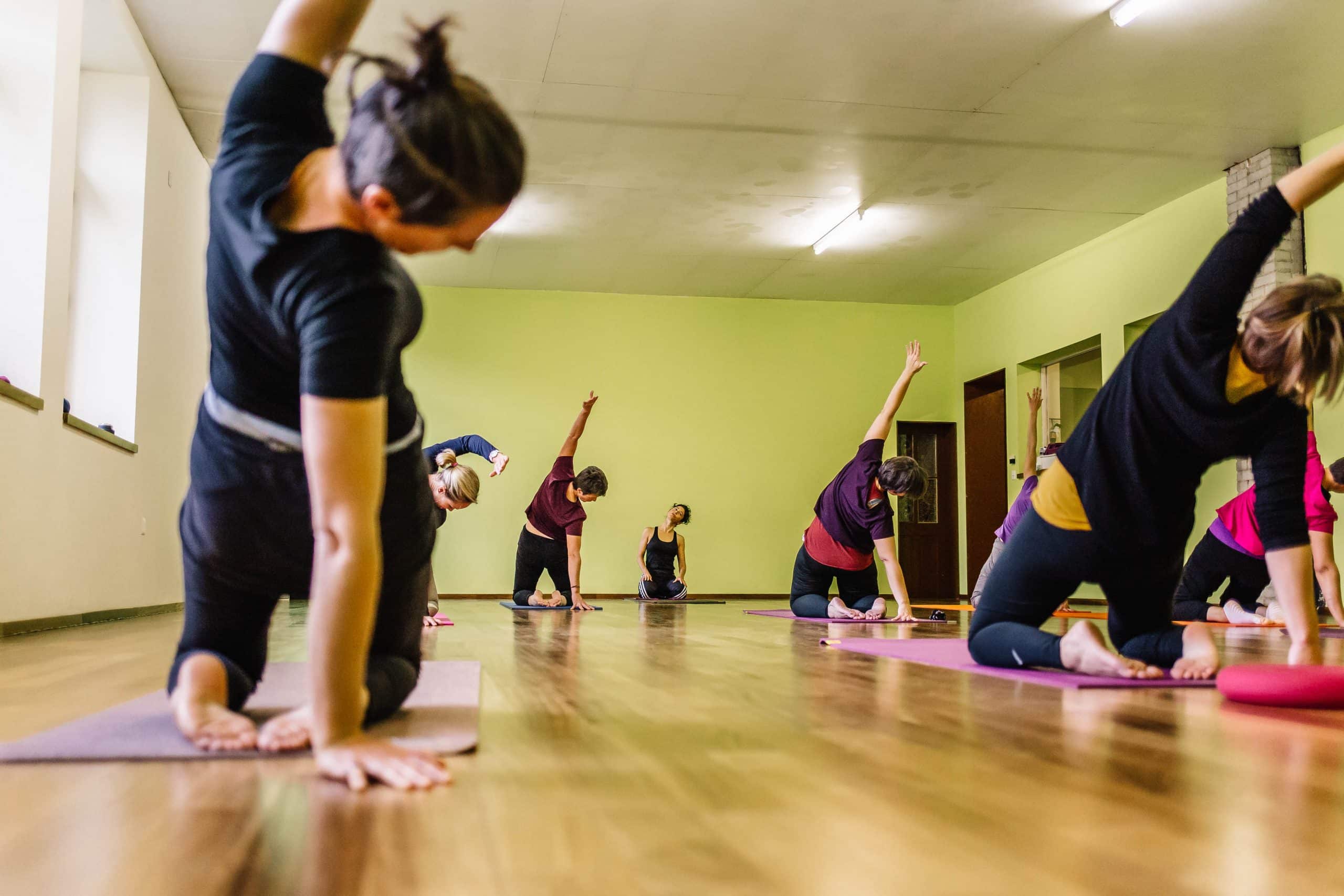 Personnes sur tapis, effectuant des étirements latéraux dans une salle lumineuse.