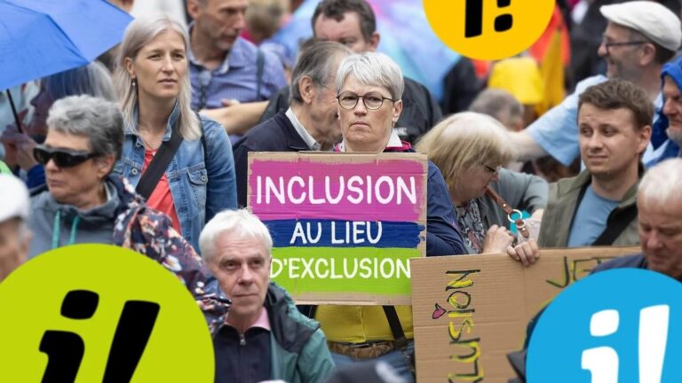 Une femme brandit, au milieu d'une foule, une pancarte sur laquelle on peut lire «La participation plutôt que l'exclusion».