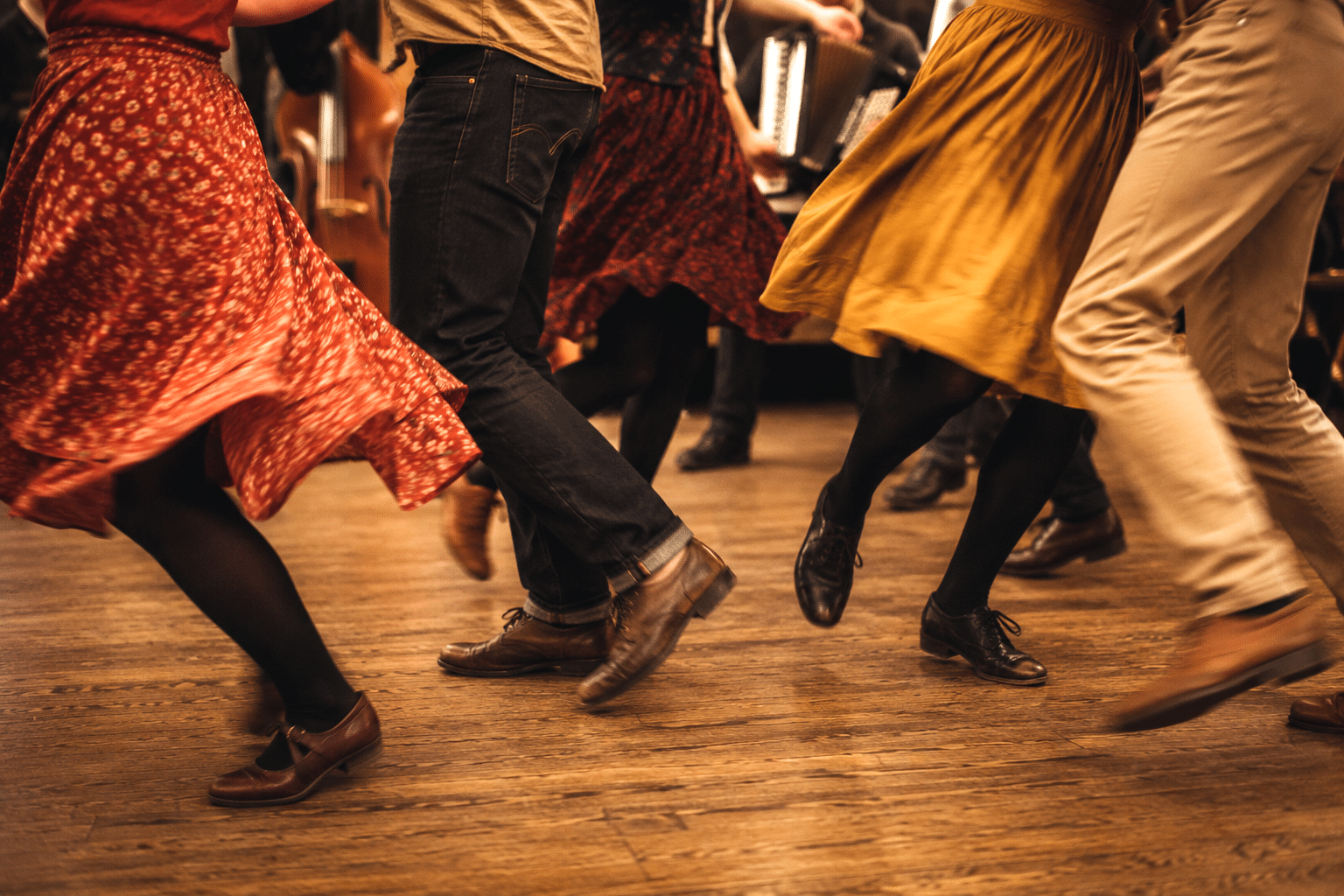 Gros plan sur les jambes et les pieds de plusieurs personnes dansant un bal folk. Les mouvements des danseurs et les vêtements en mouvement transmettent une impression d’énergie, de rythme et de convivialité. Crédit photo : générée avec ChatGPT