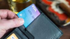 Vue rapprochée d’une main qui ouvre un porte-monnaie en cuir et sort une carte de paiement Visa. 