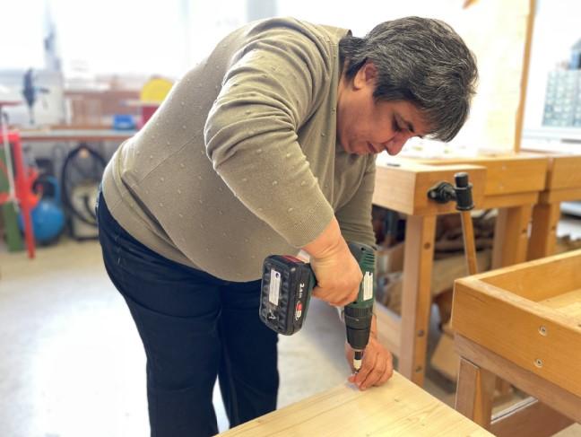 FOTO: Natalina setzt mit dem Akkuschrauber an und dreht eine Schraube in das Holzmöbelstück, welches sie für Ihre Enkelkinder selbst herstellt.