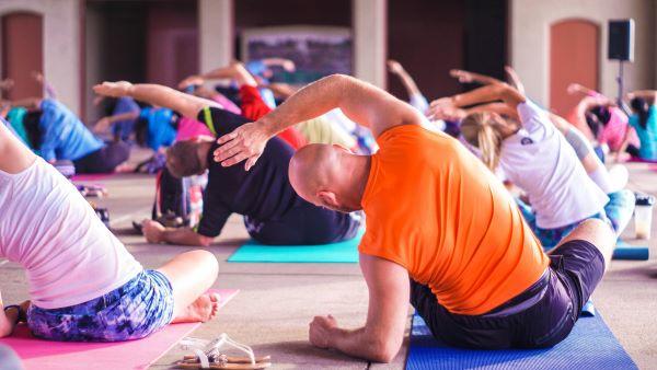 Un groupe de personnes vues de dos, faisant du yoga ou du Pilates en position assise. 