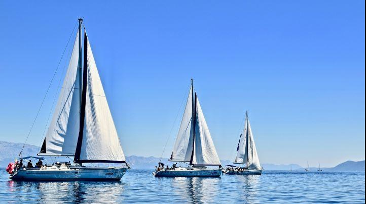 Drei Segelschiffe mit gehissten Segeln auf einem See.
