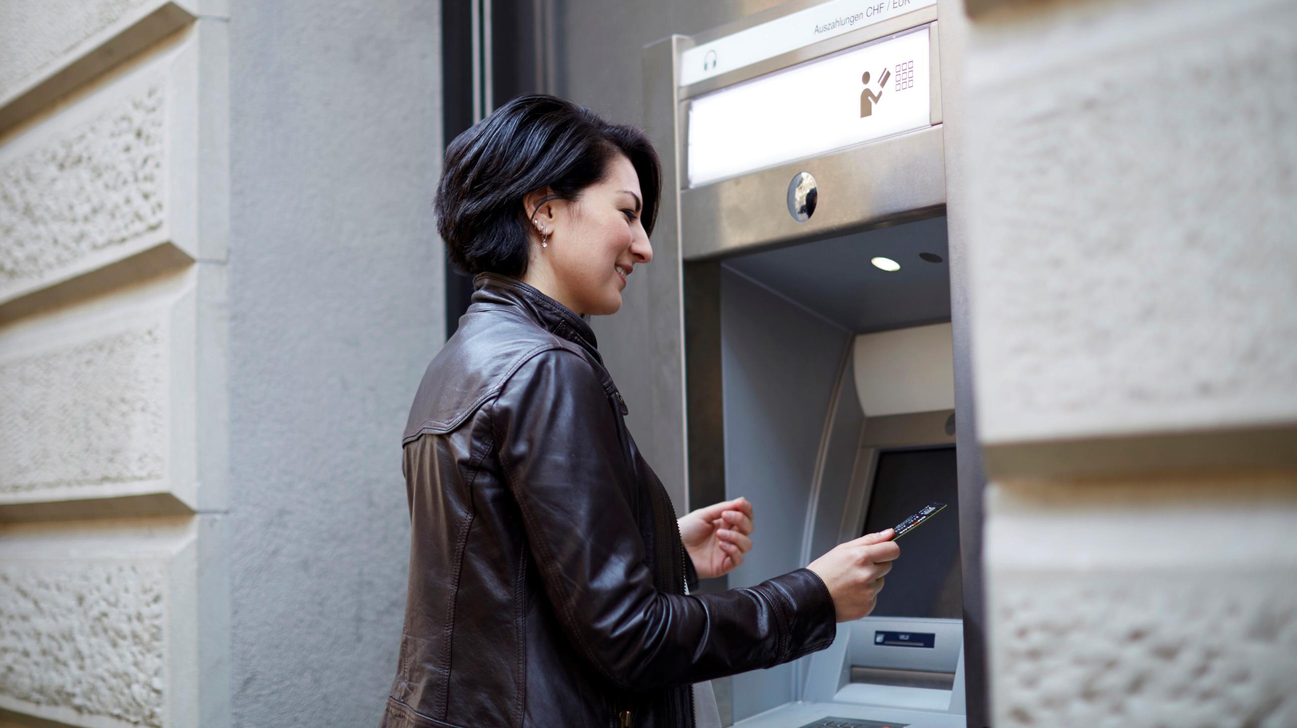 Une femme se tient devant un distributeur automatique de billets.